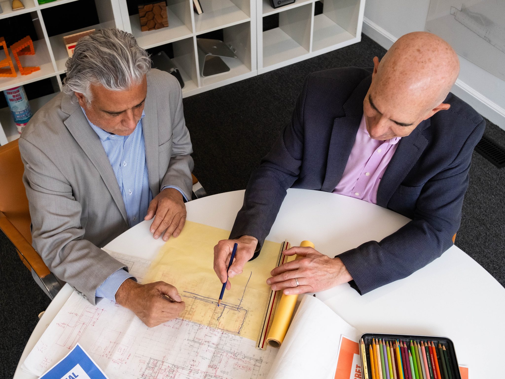 A security expert and an architect collaborate at a table, working on architectural plans and sketches.