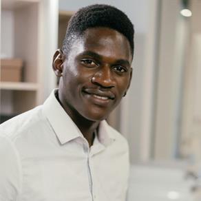 A male security officer in a white shirt smiles confidently in a well-lit office setting with blurred background details.